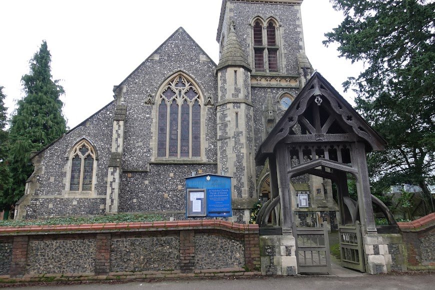 The flint frontage of St Nicholas Church seen through its timber lychgate