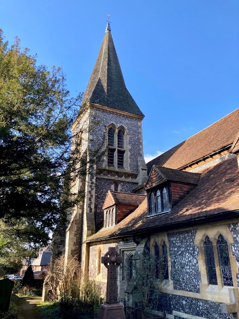 The church tower and spire with a stone Celtic cross in the foreground